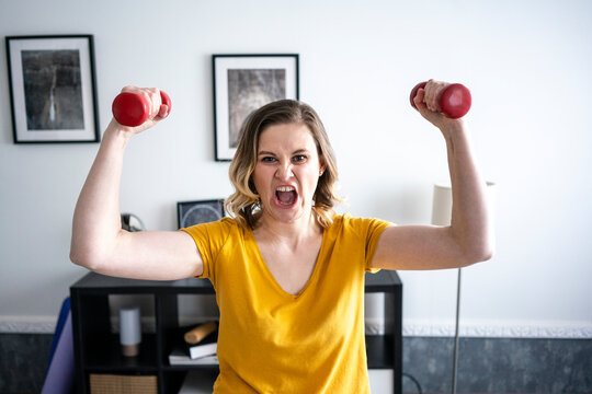 Portrait of screaming woman doing home workout with dumbbells