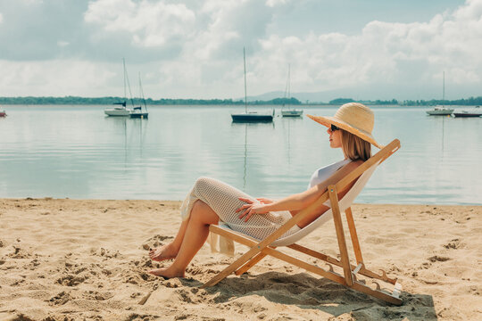 A blond woman relaxes in a deck chair on a sandy lake beach