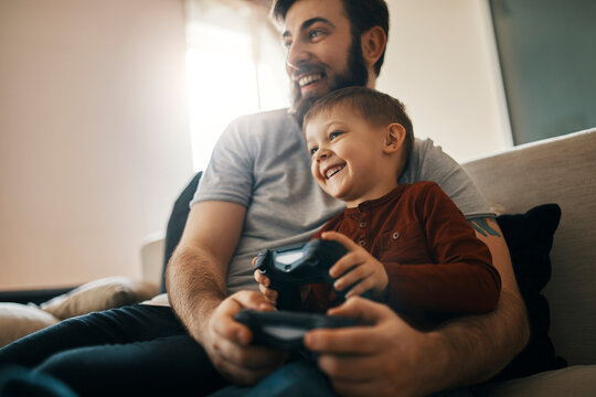 Happy father and little son sitting together on the couch playing computer game