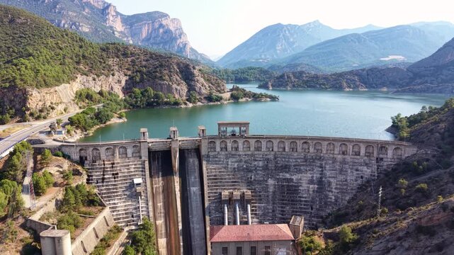 Aerial view of the arched facade and spillway of the Oliana hydroelectric dam with turquoise reservoir and mountain landscape, Segre River, Lleida, Catalonia, Spain