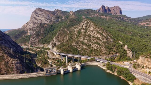 Elevated highway viaduct crossing the Segre River valley near Oliana dam, with dramatic serrated rock formations rising above forested mountain slopes in Lleida, Catalonia, Spain