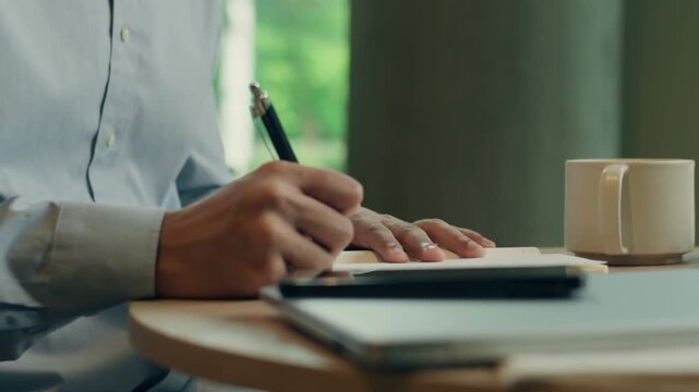 Unrecognizable business man writing notes in paper notebook unknown businessman male guy entrepreneur write information noting with pen schedule working job at table in cafe restaurant distant work