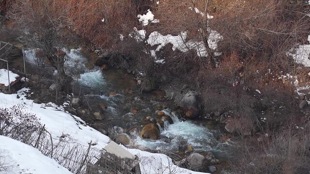 Top-down overview video with a view of a shallow narrow river with a 4-fold slower water flow with a blue tint, especially noticeable at the rapids. Winter landscapes in mountainous areas