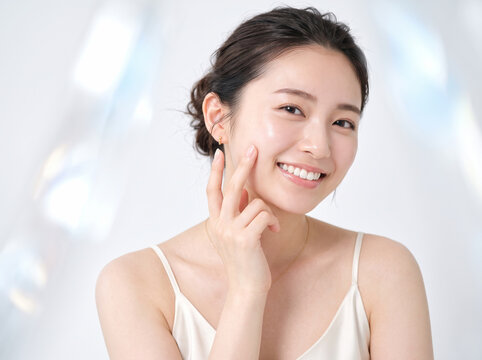 光が差し込む明るい背景で指先を頬に当てる女性