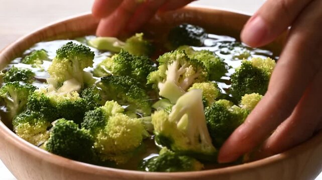 Woman hand washing fresh broccoli with clean water in a wooden bowl, meal prep