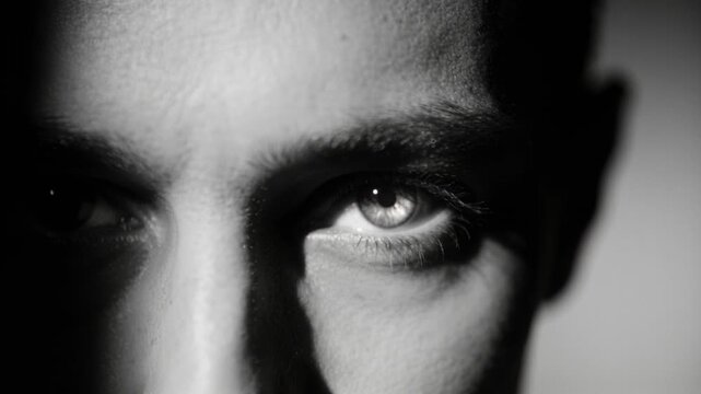 Reacting to hard light man narrowing eyes, holding gaze in studio, with right eye catchlight