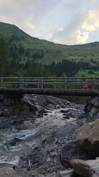 Vertical 4K shot of a person crossing a wooden bridge over an alpine river in Adelboden, Switzerland
