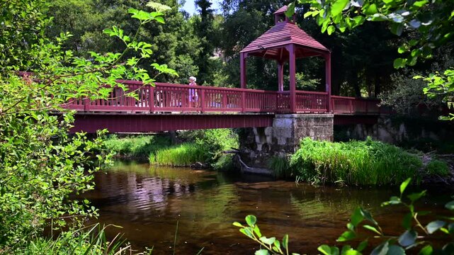 Woman waking over bridge of Cascading Waterfall Weir along the Arnoia River and Green Parklands in the Village of Allariz Galicia