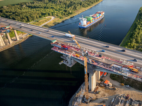 Aerial view of the Rader Hochbr&uuml;cke bridge construction over the Kiel Canal with container ship traffic in Germany.  Crane installations during the replacement construction of highway bridge. 