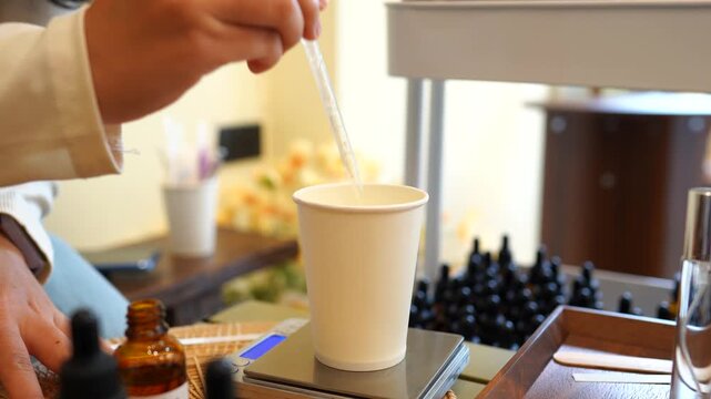 Close-up of a pipette precisely measuring essential oil into a mixing cup during handmade perfume formulation. Fragrance blending, artisan craftsmanship, DIY cosmetics, laboratory precision.