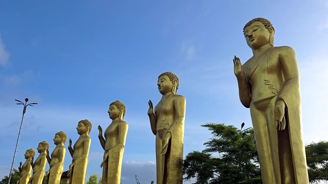 Low-angle view of golden statues of the Seven Buddhas at Nelligala International Buddhist Center in Kandy, Sri Lanka, sacred Buddhist sculptures against the sky. 4K