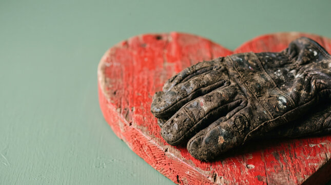 Dirty Work Gloves on a Wooden Heart Symbolizing Hard Work, Dedication and Love