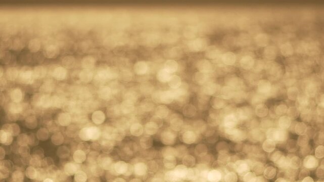 Bokeh light water shimmering abstract golden reflections on a soft sea surface create a tranquil warm glowing background for cinematic projects