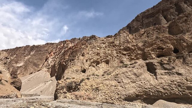 Tilt across an eroded cliff face riddled with ancient sky caves on the road to Chele, Upper Mustang, Nepal
