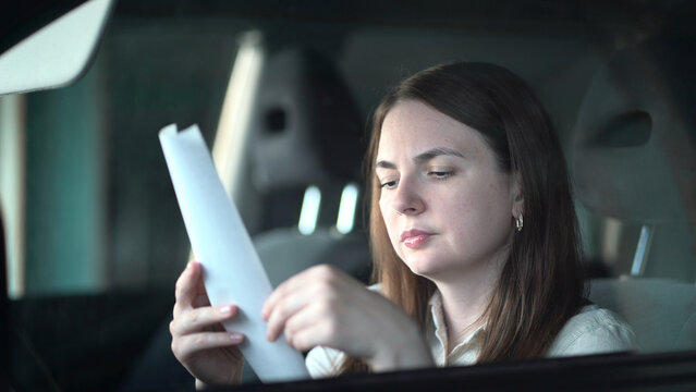 Young woman seated in a car intently examines a paper receipt detailing expensive shopping purchases while reviewing her expenses and budget.