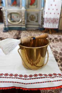 Brass bucket with holy water and an aspergillum on an embroidered towel inside an Orthodox church before baptism.
