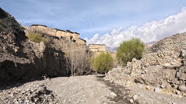 Dolly in along riverbed with dry mud brick houses on eroded cliffs. Tetang Village. Upper Mustang, Nepal