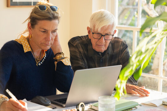adult daughter helping her elderly father with his finances using laptop