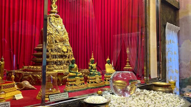 Interior view of the Holy Relic Shrine with golden Buddha statues, an ornate golden relic chamber, flowers, and incense offerings, showcasing the sacred atmosphere of Buddhist worship. 4K