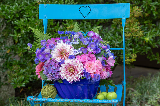 Blumen-Arrangement mit Dahlien, Rosen, Hortensienbl&uuml;ten, Federnelken, Wiesenstorchschnabel in alter Gugelhupfform auf einem Gartenstuhl
