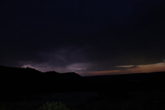 Rel&aacute;mpago intra-nube horizontal iluminando el cielo de tormenta nocturna. Paisaje dram&aacute;tico con silueta de monta&ntilde;a y espacio negativo.