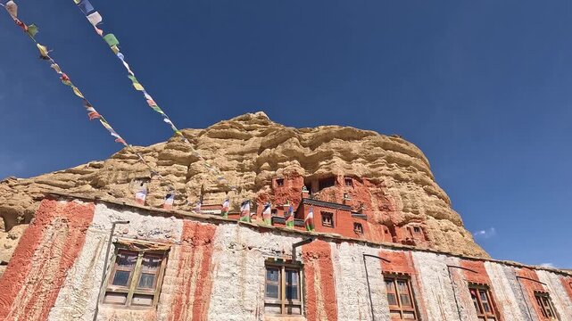 Red white cliff monastery built into rock face prayer flags Garphu Upper Mustang Nepal
