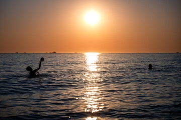 Fototapeta premium Children playing ball in ocean at sunset