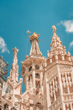 Intricate gothic marble spires on the roof of Milan Cathedral under blue sky.