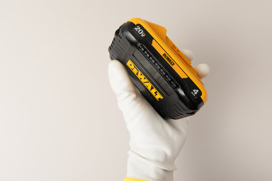 Kharkiv, Ukraine, July 12 2026: Illustrative editorial of  gloved hand holding a single DeWalt 20V MAX compact lithium-ion battery pack against a white background, showing brand labeling.