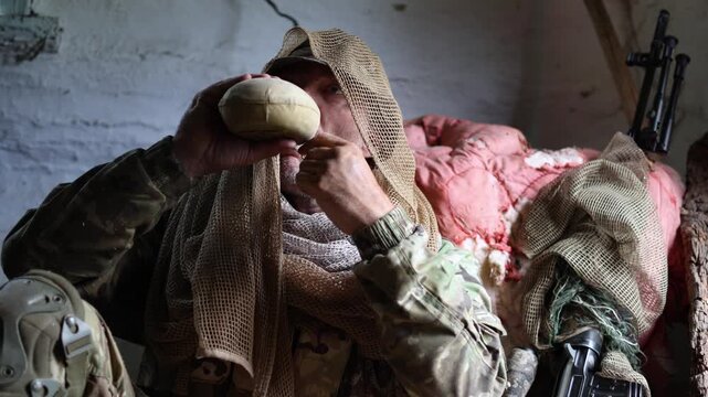 An exhausted, dirty soldier sits in a dilapidated building and drinks water from a flask. A brief respite between battles. Slow motion 4K footage.