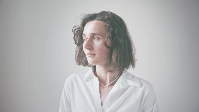 Young woman in white collared shirt posing for close-up portrait against soft neutral background, showcasing varied facial expressions and gaze directions.