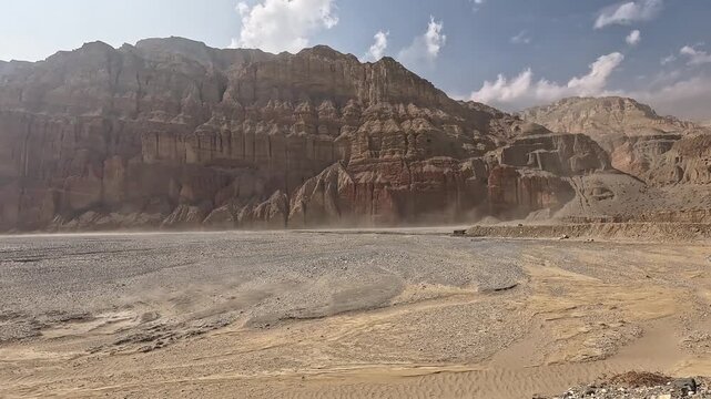 Sandstorm blowing across dry river bed, dramatic red layered cliffs, Upper Mustang Nepal