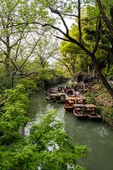Fototapeta premium Canal boats beside spring trees and flower beds at Tiger Hill Park, Suzhou, China