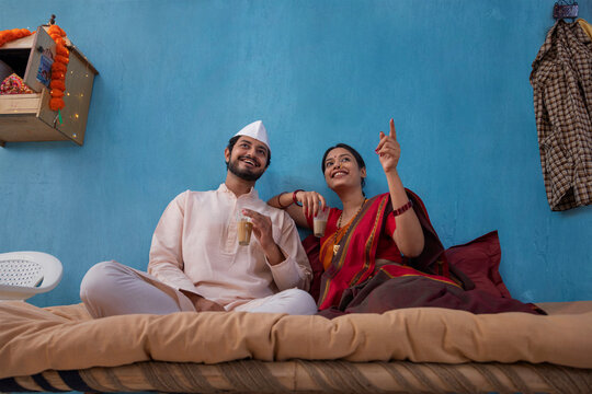 Maharashtrian couple having tea and pointing while sitting on cot at home