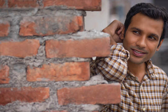 Close-up portrait of smiling young man leaning on brick wall