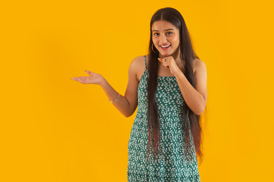 Portrait of a smiling teenage girl gesturing while standing against yellow background