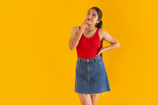 Teenage girl thinking with hand on chin against yellow background