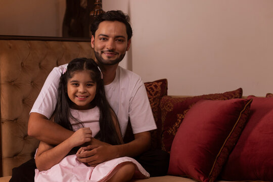 Father and daughter sitting on deewan and looking at camera