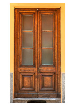 traditional vintage wooden double front door with decorative lower panels and glass windows, set against a vibrant yellow plastered wall in an old European town. Isolated