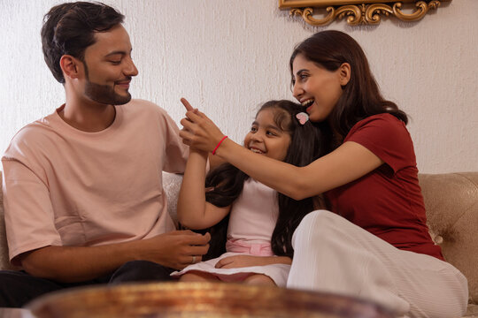 Happy young couple with their daughter having fun while sitting together on sofa at home