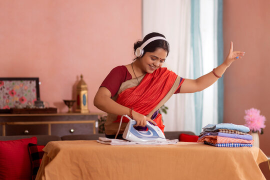 Portrait of a happy woman listening music on headphones while ironing clothes at home