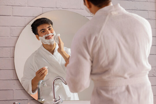 Young man applying shaving cream to his face in a bathroom at home