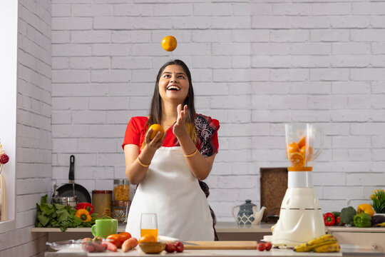 Smiling woman juggling with oranges while making juice in kitchen