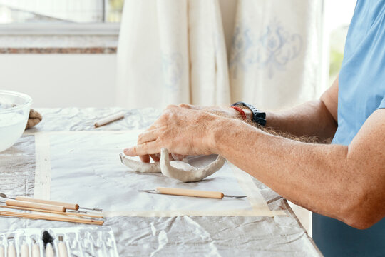Male hands sculpting clay figure at table with tools in art studio. Creative handmade pottery, workshop and hobby concept.