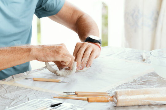 Male hands sculpting clay figure at table with tools in art studio. Creative handmade pottery, workshop and hobby concept.