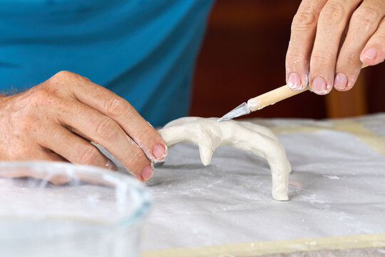 Male hands sculpting clay figure at table with tools in art studio. Creative handmade pottery, workshop and hobby concept.