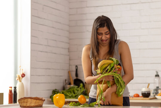 Woman standing in kitchen holding a heavy bag of vegetables