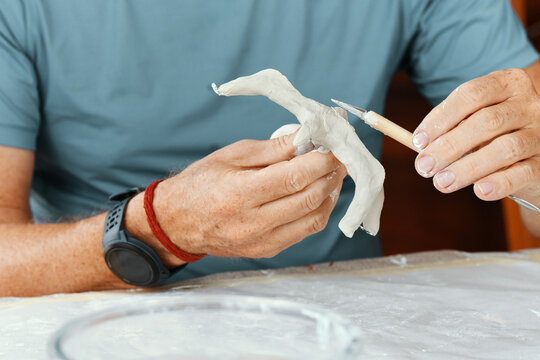 Male hands sculpting clay figure at table with tools in art studio. Creative handmade pottery, workshop and hobby concept.