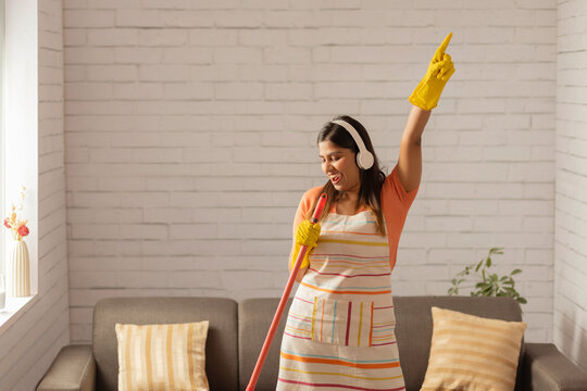 Cheerful woman dancing while sweeping floor with broom 