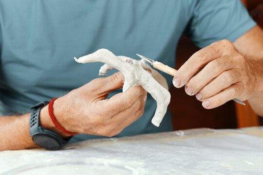 Male hands sculpting clay figure at table with tools in art studio. Creative handmade pottery, workshop and hobby concept.